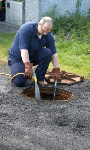 Technicien en train de curer une canalisation extérieure avec un jet d’eau haute pression